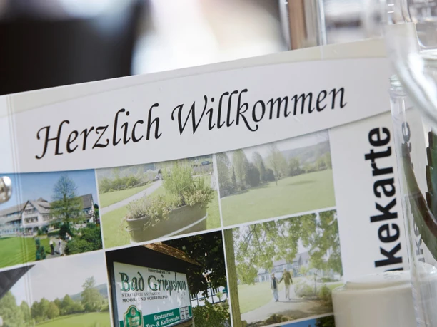 Hotel-Bad-Griepshop Menükarte mit der Aufschrift "Herzlich Willkommen" in einem Hotelrestaurant, neben einem Weißweinglas.