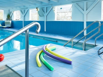 Hotel-Bad-Griepshop Innenbereich eines Hallenbads mit blauen Fliesen, Liegestühlen und Schwimmutensilien am Poolrand.