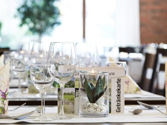 Hotel-Bad-Griepshop Festlich gedeckter Tisch mit Weingläsern, gefalteten Servietten und kleiner Pflanze in hellem Raum.