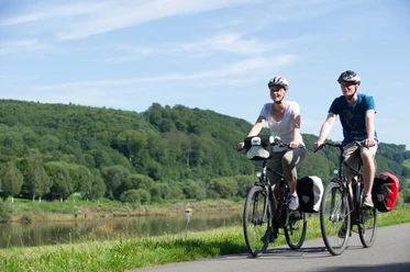 Mit dem Fahrrad entlag der Weser unterwegs Zwei Personen radeln auf einem Fahrradweg entlang der Weser, umgeben von üppigen, grünen Wäldern.