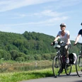 Mit dem Fahrrad entlag der Weser unterwegs Zwei Personen radeln auf einem Fahrradweg entlang der Weser, umgeben von üppigen, grünen Wäldern.