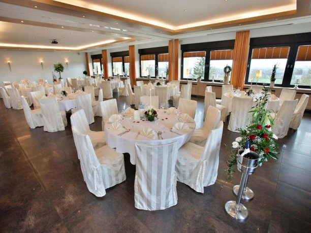 Hotel Wiehentherme Großer, eleganter Bankettsaal mit runden, weiß eingedeckten Tischen und großen Fenstern.