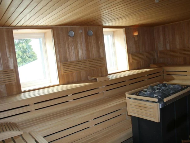 Hotel Wiehentherme Holzverkleidete Sauna mit zwei Fenstern und holzbasierten Sitzbänken, im Vordergrund ein Saunaofen.