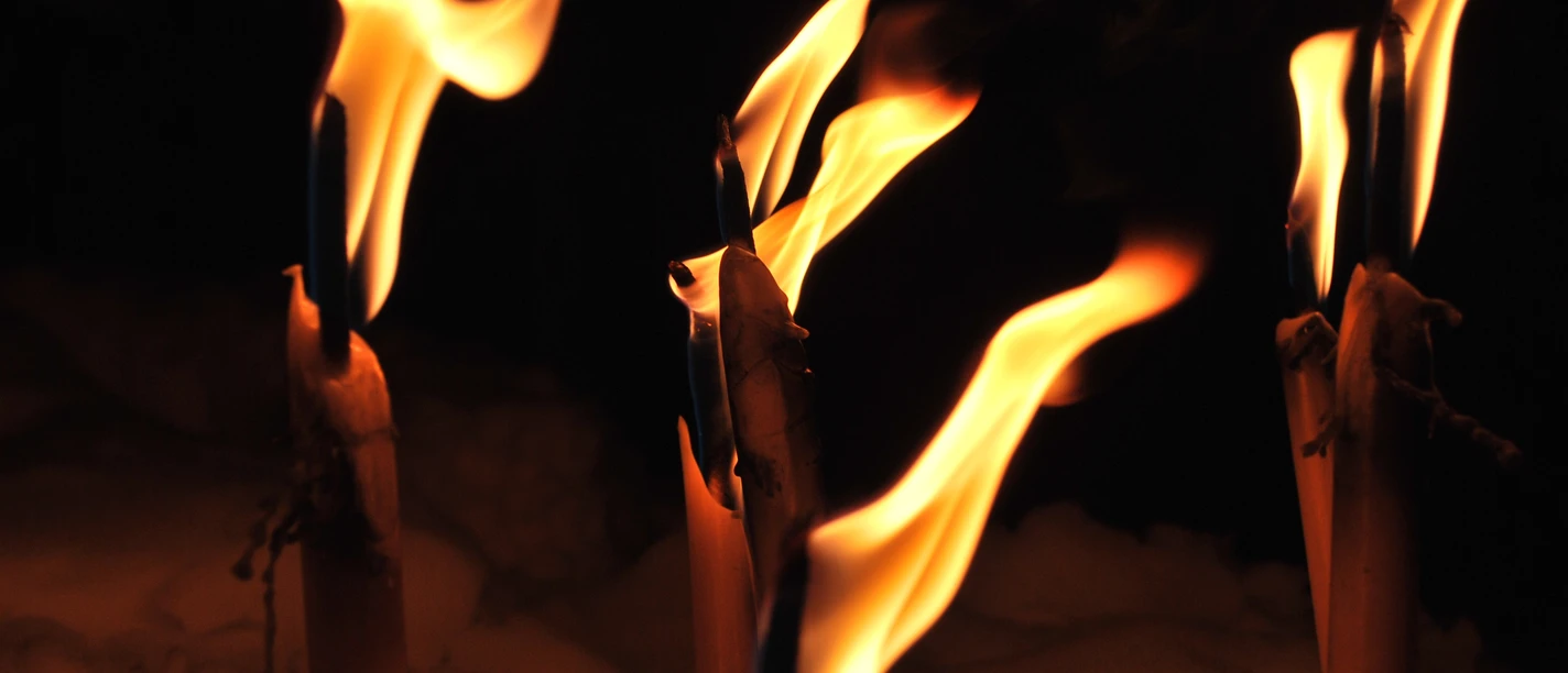 Brennende Fackeln mit hellen Flammen vor dunklem Hintergrund.
