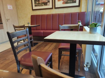 Eine Sitzecke in einem Café, Stühle und Bank sind mit rotem Leder bezogen, das Holz ist dunkel