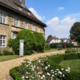Historisches Schloss Gehrden mit gepflegten Hecken und blühenden Rosen im sonnigen Garten.