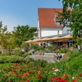 Ein modernes Café mit Sonnenschirmen und Terrasse, umgeben von üppiger, blühender Gartenanlage.
