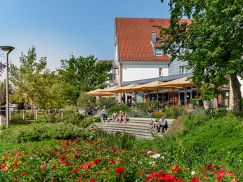Ein modernes Café mit Sonnenschirmen und Terrasse, umgeben von üppiger, blühender Gartenanlage.