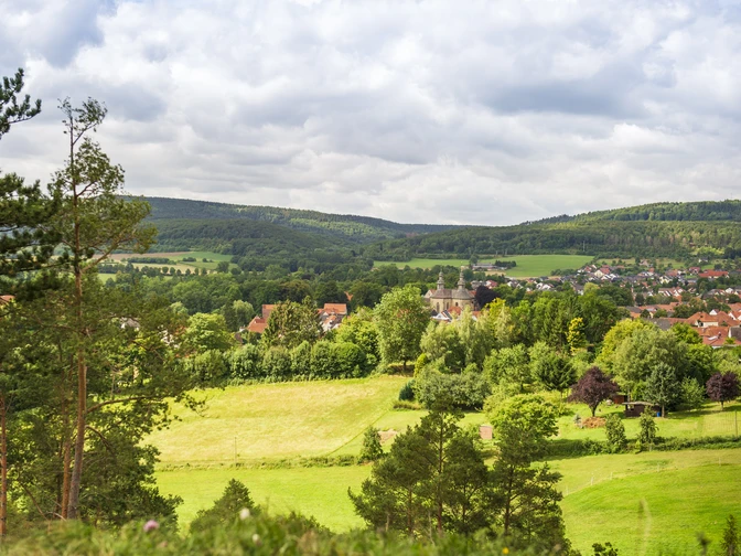Blick auf Schloss Willebadessen inmitten grüner Landschaft, umgeben von bewaldeten Hügeln und Feldern.