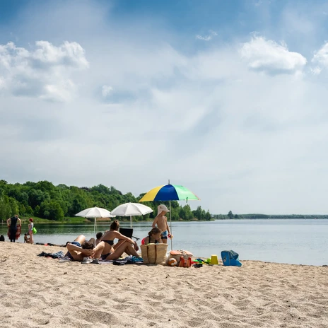 Eine Familie mit Kindern sitzt in Badekleidung im Sommer am Sandstrand des Cospudener Sees, rundherum gehen Menschen Baden und genießen die Sonne, Familie, Leipzig mit Kindern, Freizeit, Leipziger NeuseenlandA family with children in swimwear sits on the sandy beach of Lake Cospuden in summer, all around people go swimming and enjoy the sun, Family, Leipzig with children, Leisure, Leipzig New Lake DistrictRodina s dětmi v plavkách sedí v létě na písečné pláži jezera Cospuden, všude kolem se lidé koupou a užívají si slunce, Rodina, Lipsko s dětmi, Volný čas, Lipsko Nová Jezerní oblastRodzina z dziećmi w strojach kąpielowych siedzi latem na piaszczystej plaży jeziora Cospuden, dookoła ludzie pływają i cieszą się słońcem, Rodzina, Lipsk z dziećmi, Wypoczynek, Lipsk Nowe PojezierzeEen gezin met kinderen in zwemkleding zit op het zandstrand van het Cospudenmeer in de zomer, rondom gaan mensen zwemmen en genieten van de zon, Familie, Leipzig met kinderen, Vrije tijd, Leipzig Nieuw MerengebiedUna famiglia con bambini in costume da bagno siede sulla spiaggia sabbiosa del lago Cospuden in estate, le persone intorno fanno il bagno e si godono il sole, Famiglia, Lipsia con bambini, Tempo libero, Lipsia Nuovo Distretto dei Laghi
