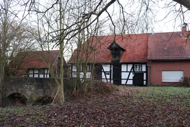 Fachwerkgebäude mit rotem Ziegeldach und Brücke im herbstlichen Wald bei der Ellerburger Mühle.