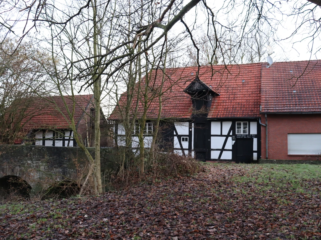 Fachwerkgebäude mit rotem Ziegeldach und Brücke im herbstlichen Wald bei der Ellerburger Mühle.