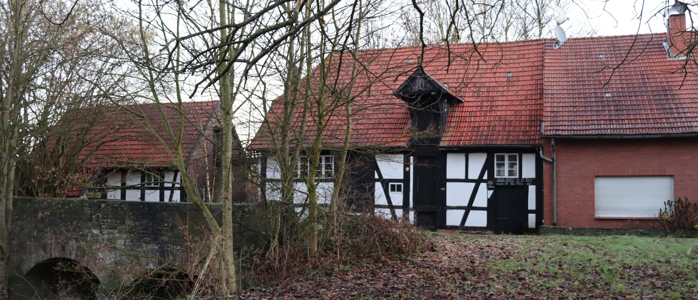 Fachwerkgebäude mit rotem Ziegeldach und Brücke im herbstlichen Wald bei der Ellerburger Mühle.