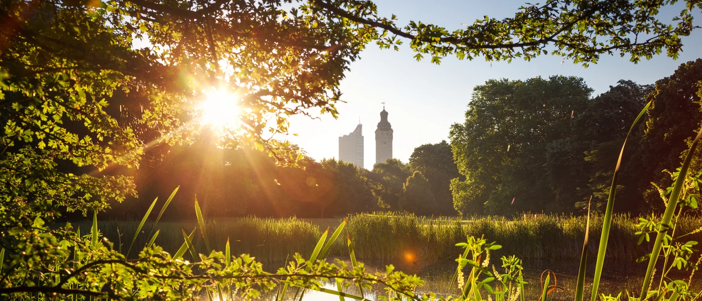 Słoneczny widok z brzegu stawu w Johannparku, przez zieleń, na Nowy Ratusz i wieżowiec Cityhochhaus w Lipsku, Zielone Lipsk, czas wolny, parki