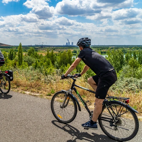 Dwóch rowerzystów na asfaltowej ścieżce wokół jeziora Störmthal, w tle przyroda i Park Technologiczny Górnictwa, Sport, Aktywnie, Kolarstwo, Region, Leipziger Neuseenland