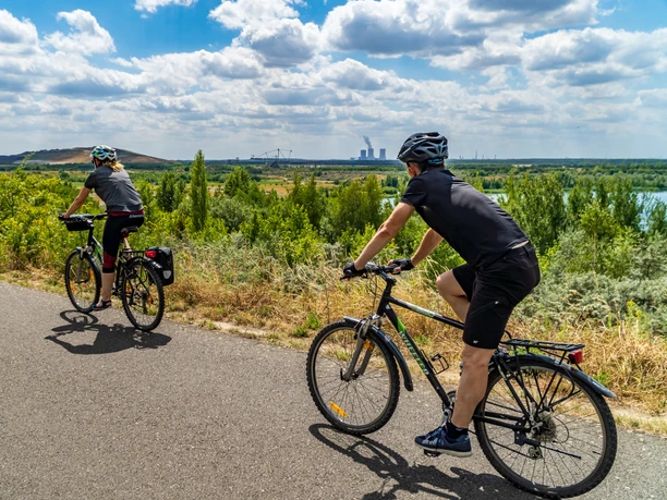 Dwóch rowerzystów na asfaltowej ścieżce wokół jeziora Störmthal, w tle przyroda i Park Technologiczny Górnictwa, Sport, Aktywnie, Kolarstwo, Region, Leipziger Neuseenland