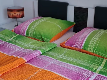 Schlafgelegenheit Zwei Einzelbetten mit bunter Bettwäsche und Nachttischlampe in einem schlichten Gästezimmer.