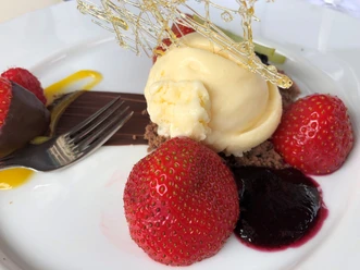 Eis Dessert Vanilleeis auf Schokoladenboden, umgeben von frischen Erdbeeren und Beerenpüree, garniert mit filigranem Karamell.