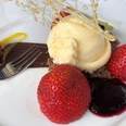 Eis Dessert Vanilleeis auf Schokoladenboden, umgeben von frischen Erdbeeren und Beerenpüree, garniert mit filigranem Karamell.