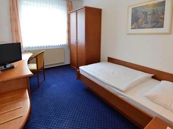 Zimmer Ein schlicht eingerichtetes Einzelzimmer mit Holzmöbeln, blauem Teppich und einem Schreibtisch.