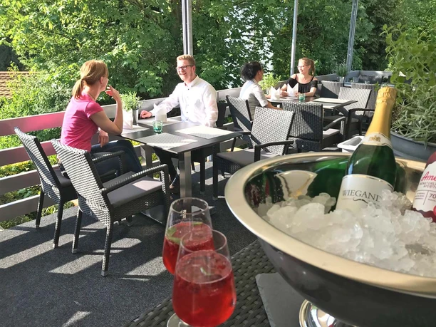 Einladende Terrasse Menschen genießen ein Gespräch auf einer sonnigen Terrasse, umgeben von grüner Vegetation.