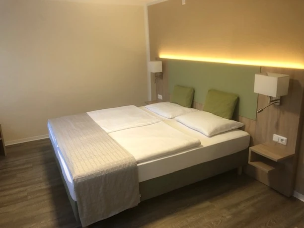 Ein Doppelbett mit hellem Holzrahmen, zwei Wandlampen und modernen Kopfteilleuchten in einem ruhigen Zimmer.