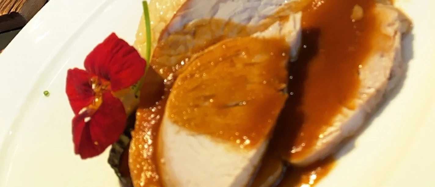 Dish of fine meat in hearty gravy, garnished with flower and vegetables on a white plate.