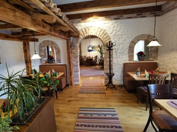 Ein Restaurantinnenraum mit Holzbalken, Steinelementen und Pflanzen; einladende Sitzbereiche unter Lampen.