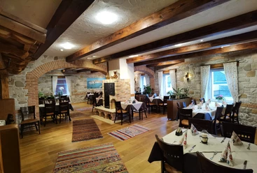 Ein rustikales Restaurant mit Holzbalkendecke und Steinwänden; bunt gemusterte Teppiche zieren den Boden.