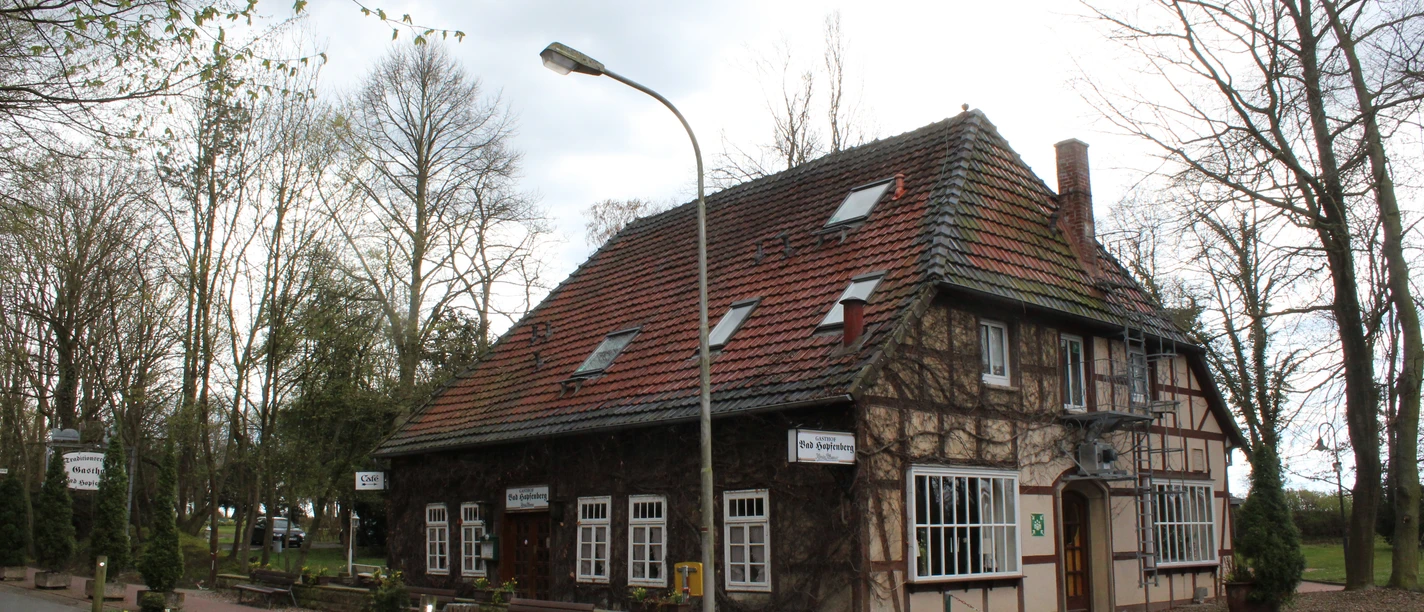 Gasthof Bad Hopfenberg Historischer Gasthof mit rotem Ziegeldach und Fachwerkdetails, umgeben von Bäumen und Blumenbeeten.