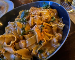 Nudeln Hausgemachte Bandnudeln mit cremiger Sauce, frischen Kräutern und Käsespänen in blauer Schale.