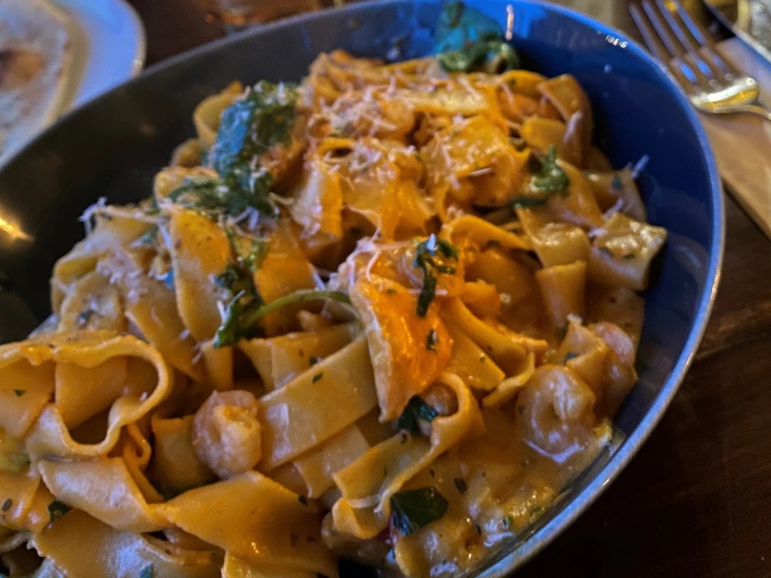 Nudeln Hausgemachte Bandnudeln mit cremiger Sauce, frischen Kräutern und Käsespänen in blauer Schale.