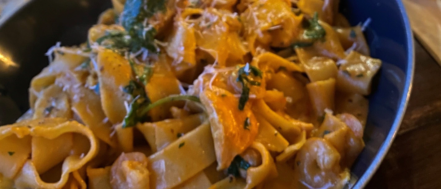 Nudeln Hausgemachte Bandnudeln mit cremiger Sauce, frischen Kräutern und Käsespänen in blauer Schale.