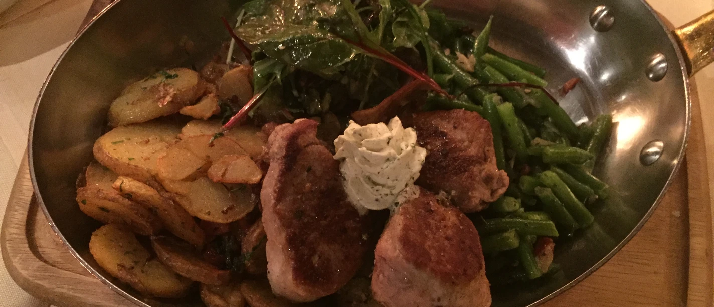 Een pangebakken gerecht met knapperig gebakken aardappelen, sappig vlees, bonen en slablaadjes.