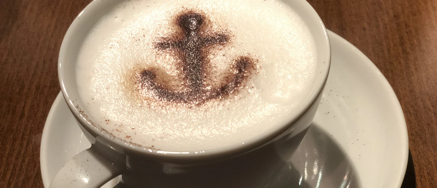 Cappuccino with cocoa motif of an anchor on milk foam, served on a wooden table.