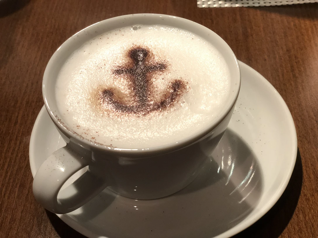 Kaffee Cappuccino mit Kakaomotiv eines Ankers auf Milchschaum, serviert auf einem Holztisch.