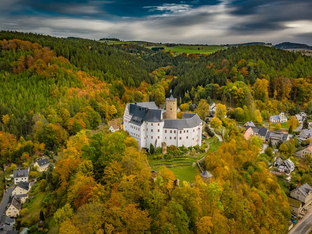 Aerial view of a castle surrounded by autumnal forests and a small village.