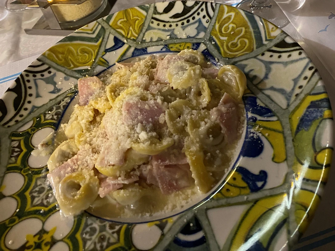 Nudelgericht Ein Teller gefüllt mit Tortellini und Schinkenstücken, bedeckt mit einer cremigen Käsesauce.