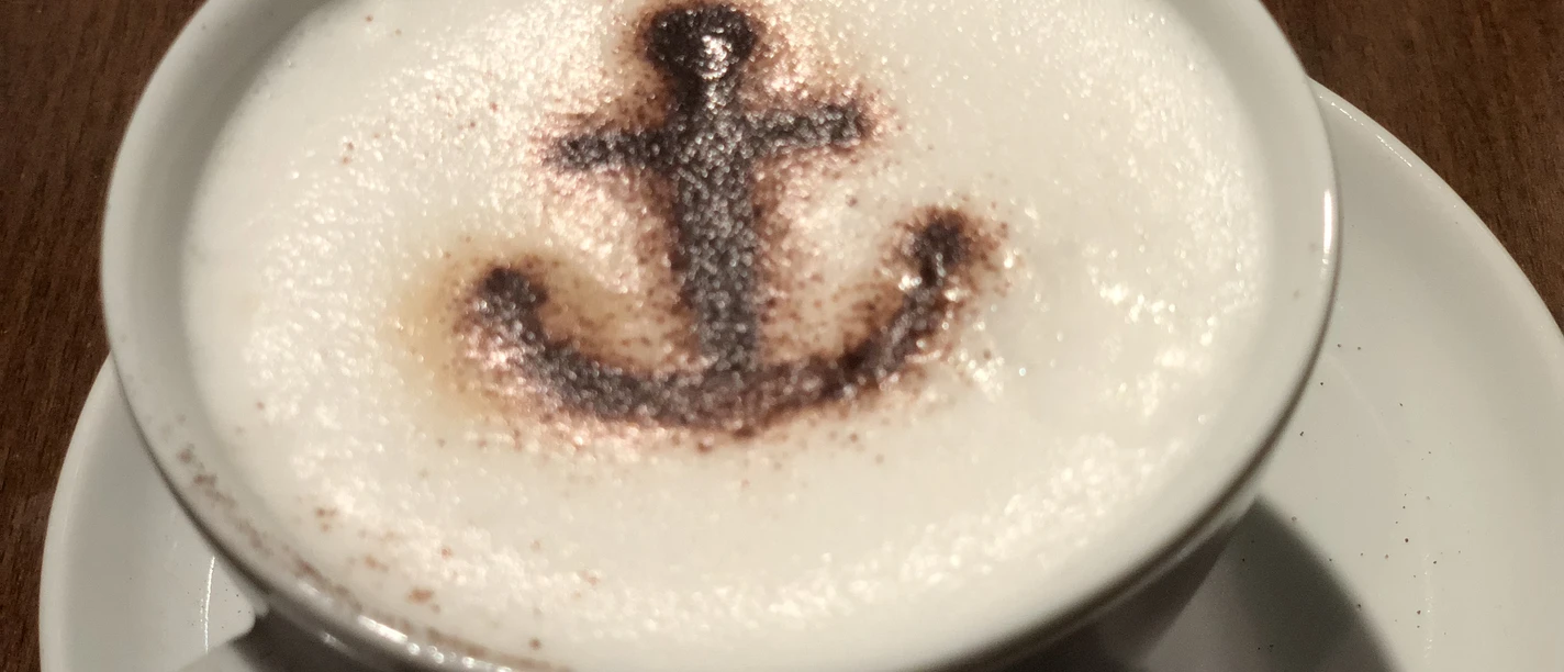 Een witte koffiekop met melkschuim en een anker van cacaopoeder als decoratie.