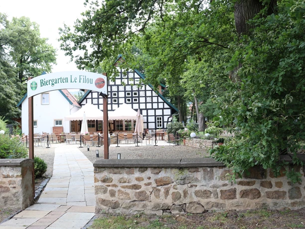 Hotel Filou Eingang zum großzügigen Biergarten des Hotels Filou mit Fachwerkhaus im Hintergrund und Bäumen.
