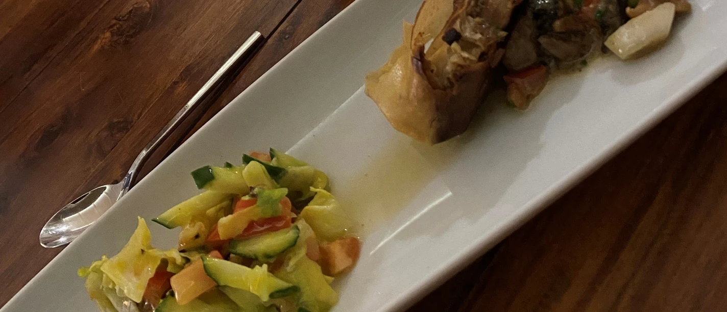 A rectangular plate presents a colorful mix of vegetables and hearty meat rolls on a wooden surface.