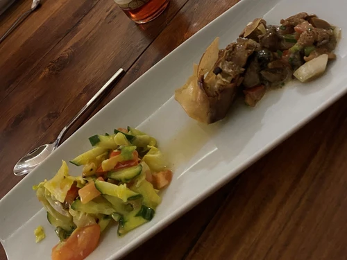 A rectangular plate presents a colorful mix of vegetables and hearty meat rolls on a wooden surface.