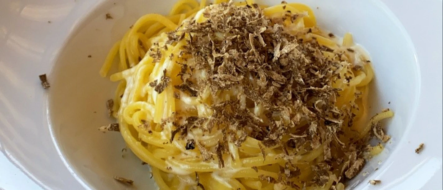 Ein tiefes weißes Tellergericht mit Spaghetti, cremiger Soße und gehobelten Trüffeln darauf.