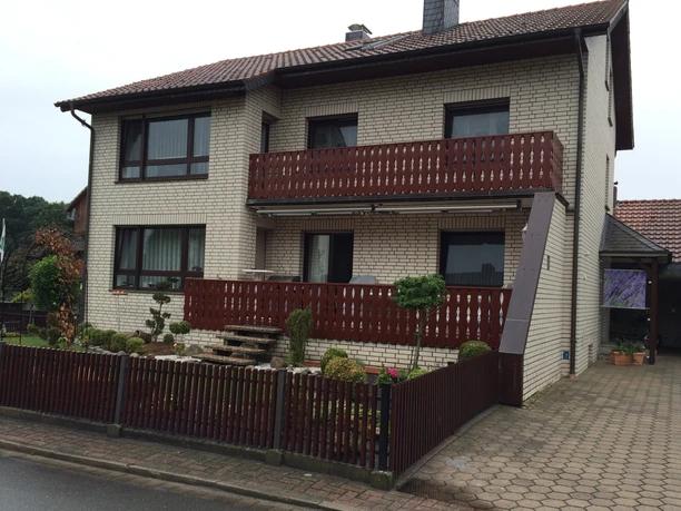 Gaestehaus-Witting_1.jpg Zweistöckiges Gästehaus mit Backsteinfassade, überdachtem Balkon und kleinem Vorgarten mit Zaun.