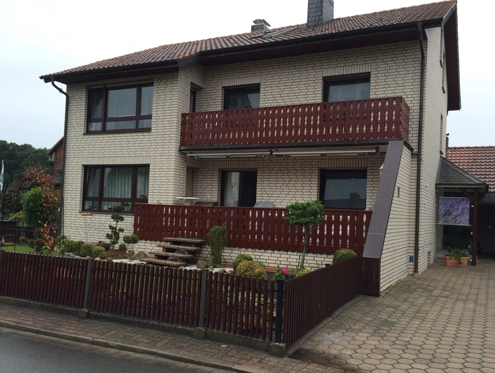 Gaestehaus-Witting_1.jpg Zweistöckiges Gästehaus mit Backsteinfassade, überdachtem Balkon und kleinem Vorgarten mit Zaun.