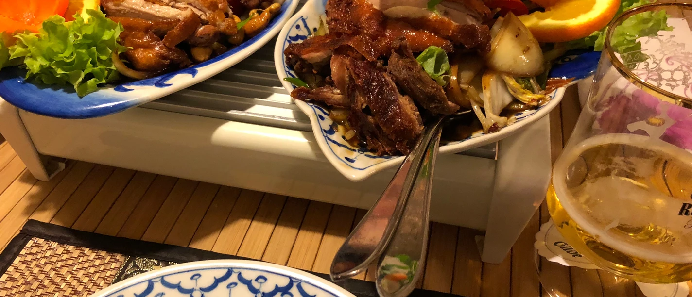 Crispy roasted duck dish on a porcelain plate with fresh orange slices and vegetable garnish.