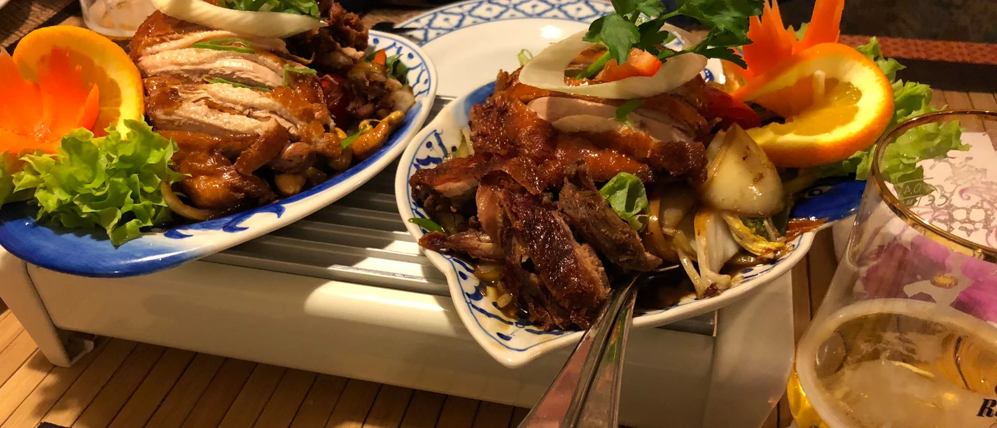 Crispy roasted duck dish on a porcelain plate with fresh orange slices and vegetable garnish.