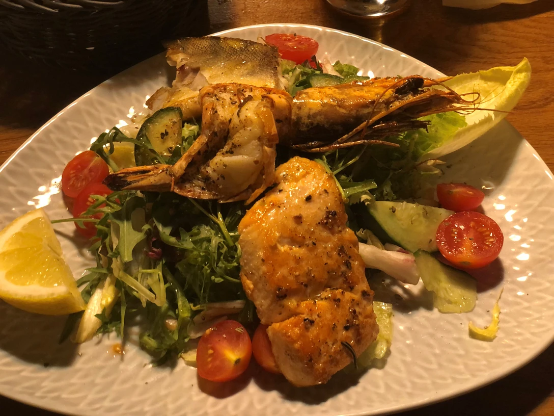 Ein Teller mit gebratenem Fisch, Riesengarnele und frischem Gemüsesalat aus Tomaten und Gurken.