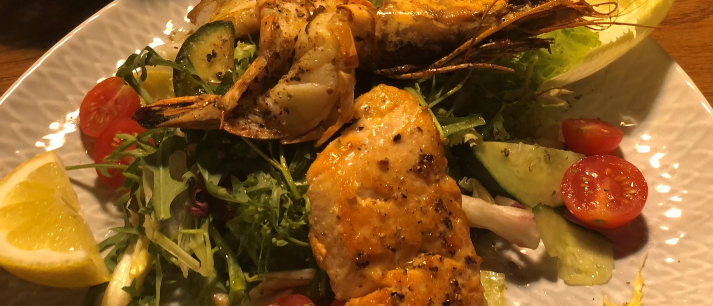 Salat und Fisch Ein Teller mit gebratenem Fisch, Riesengarnele und frischem Gemüsesalat aus Tomaten und Gurken.