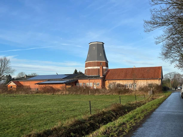 Wesermühle GbR Historische Windmühle mit rotem Ziegelbau in einer grünen Landschaft unter blauem Himmel.